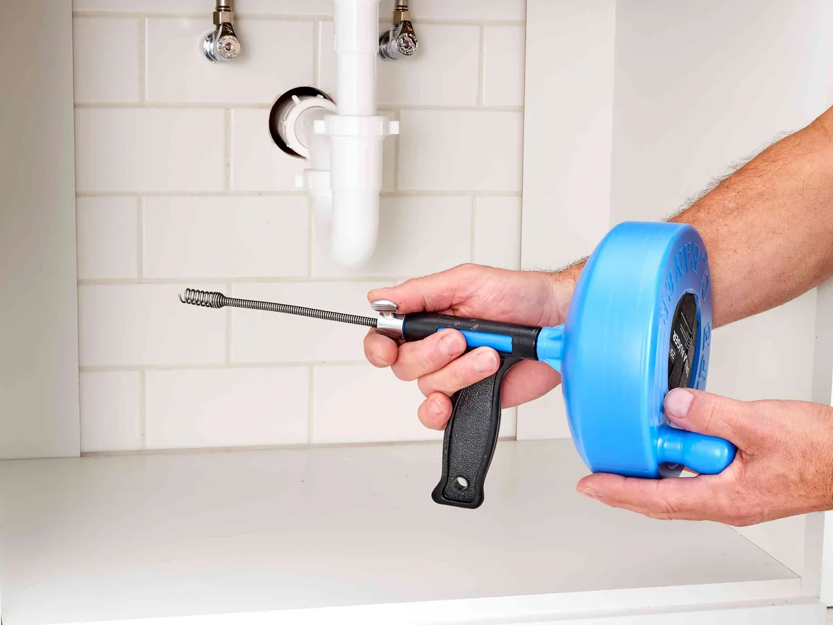 Hands feeding a drum auger cable into a bathroom drain