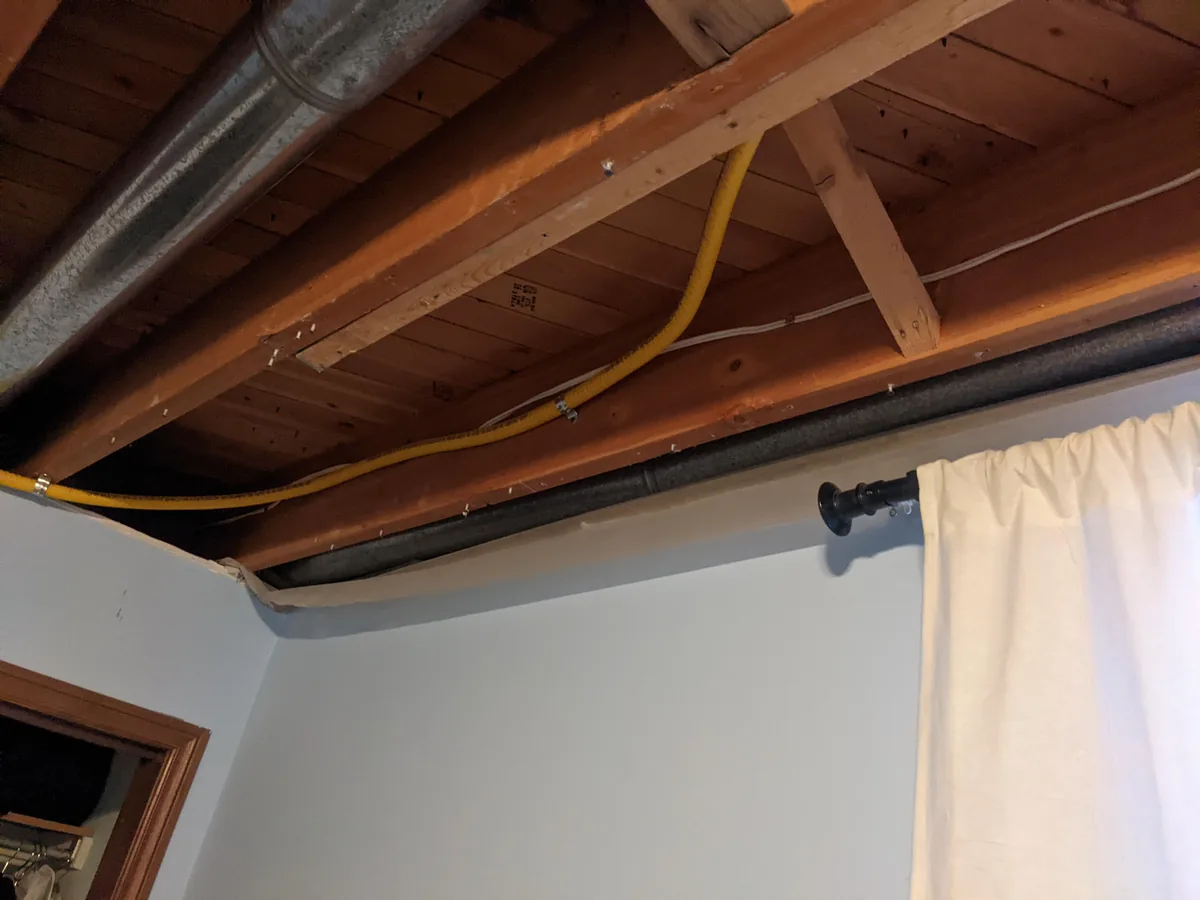 Yellow flexible gas line run along the floor joists of a basement
