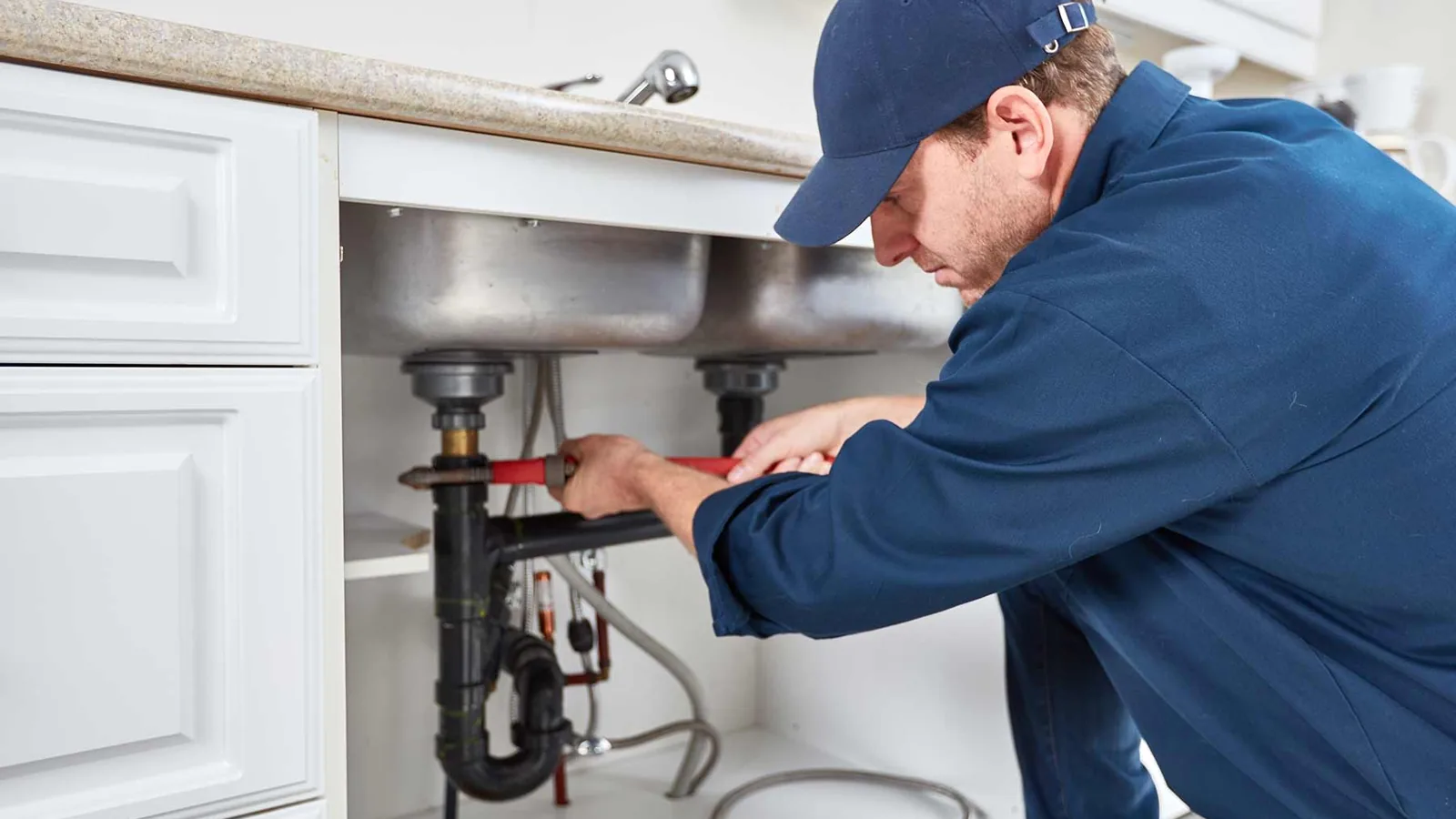 Plumber tightening a wrench on the drain pipes under a kitchen sink