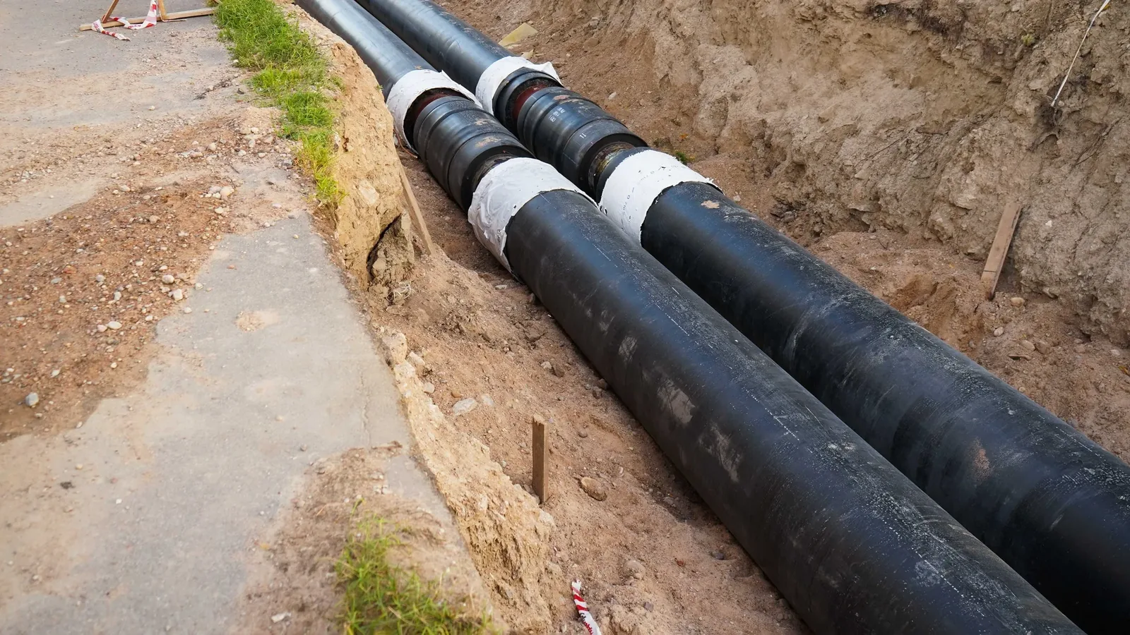 New pipe laid the length of an open trench beside a road