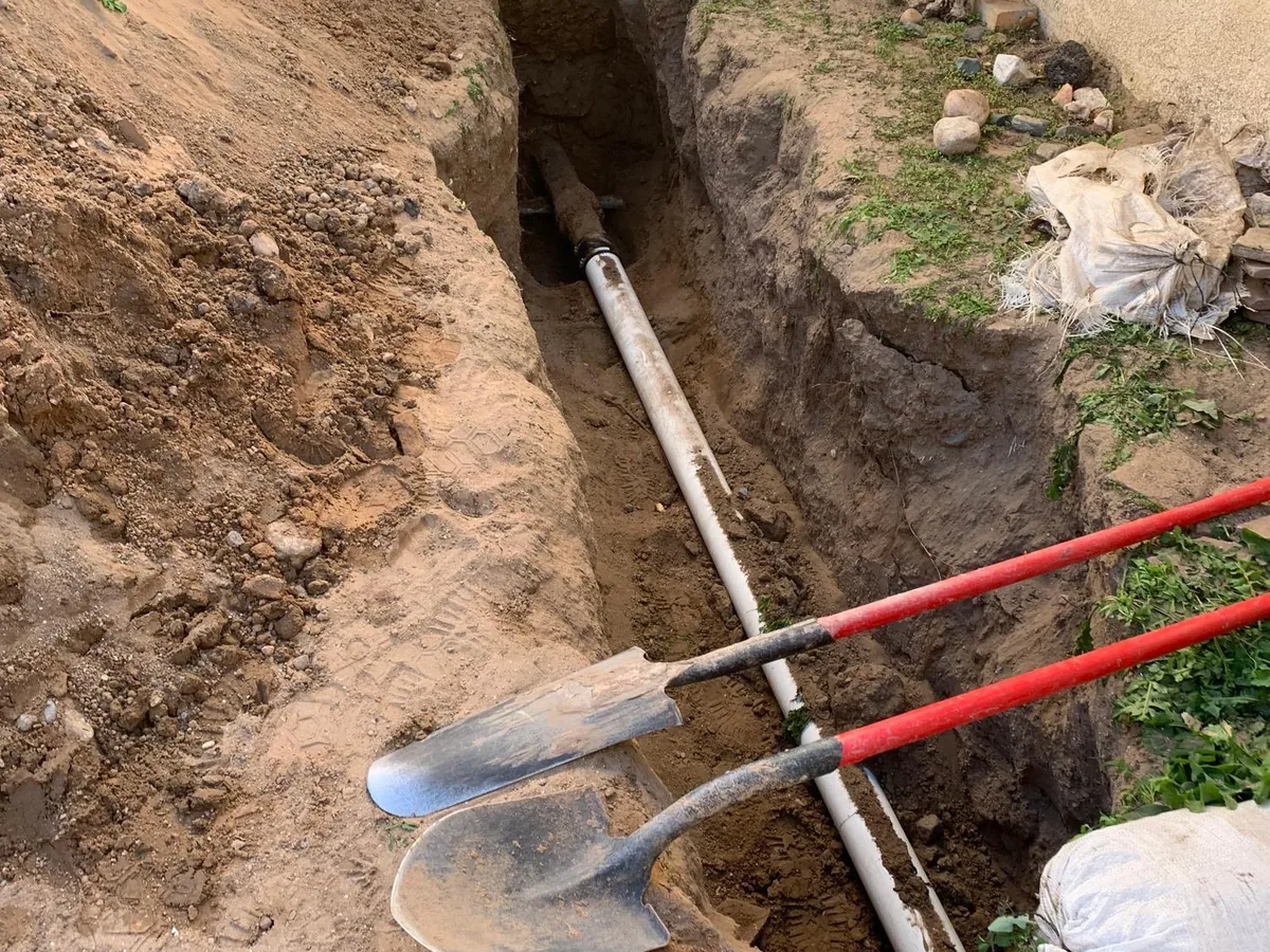 Excavated sewer lateral trench with new pipe running alongside a stucco house foundation in New Mexico