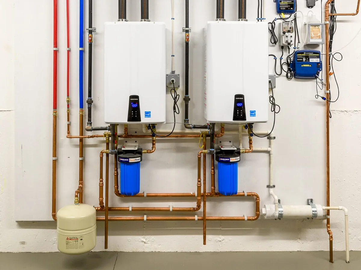 Two wall-mounted tankless water heaters with copper piping and filters