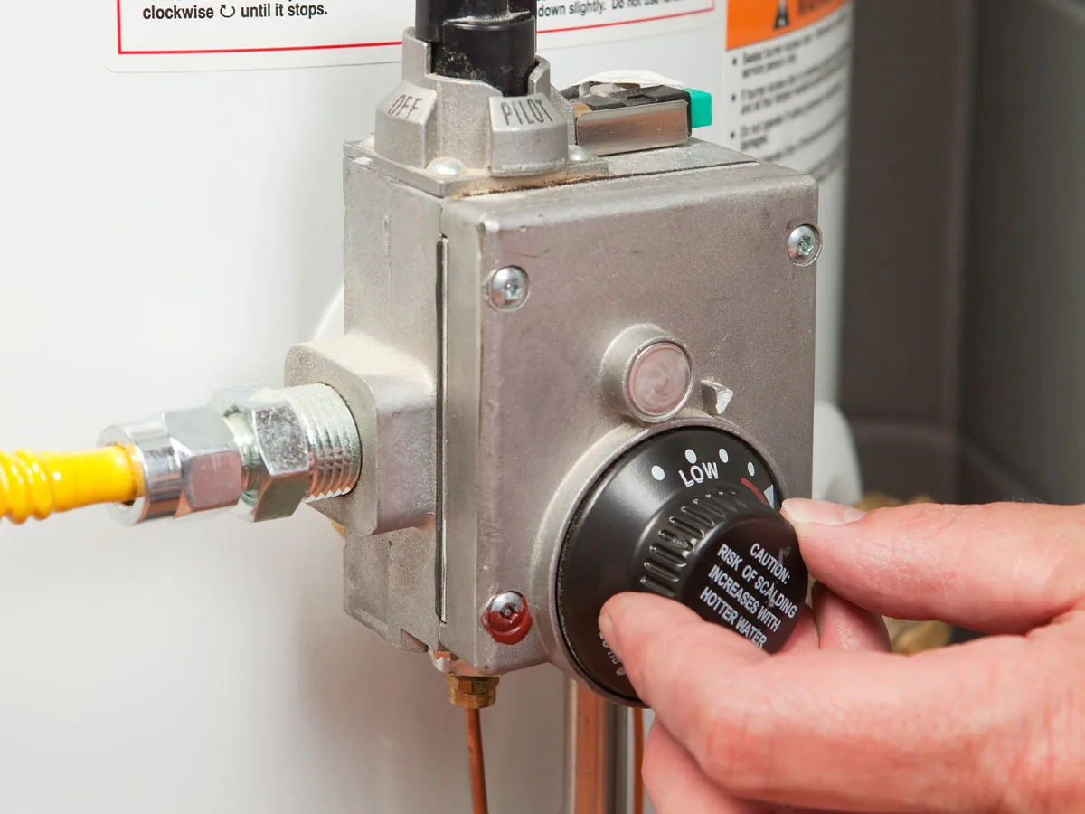 Hand adjusting the gas control valve on a tank water heater